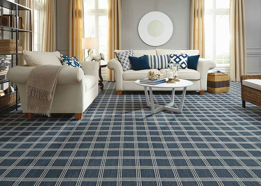 Living room with white sofas covered in blue throw pillows, and a white coffee table on blue and white tiled carpet.